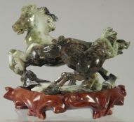 A CHINESE CARVED GREEN HARDSTONE GROUP OF HORSES, on a fitted hardwood stand, 17cm wide.