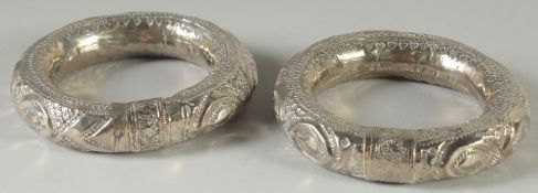 A PAIR OF ISLAMIC SILVER BANGLES, with embossed decoration, weight 130g (including beads inside