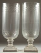 A PAIR OF GLASS STORM LAMPS with cross hatch on a square base. 15.5ins high.