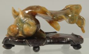 A CARVED COLOURED JADE FISH. 3ins long on a wooden base.