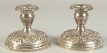 A PAIR OF SILVER EMBOSSED ROUND CANDLESTICKS. 3.5ins high.