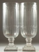 A PAIR OF GLASS STORM LAMPS with garlands on a square base. 15.5ins high.