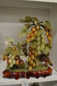 A Chinese hardstone group of grapes and vine on a wooden stand.