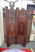 An Eastern carved and pierced hardwood four panel dressing screen with ornate brass inlaid