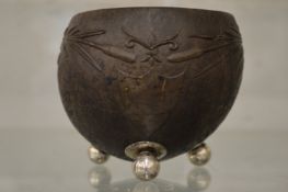 A carved coconut cup on three silver feet.