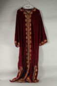 AN ARAB CRIMSON VELVET HOUSE COAT / ROBE, with gold braided decoration.