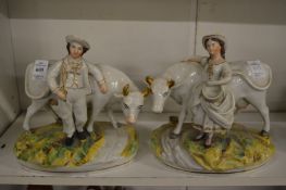 A pair of Staffordshire figures of farmer and milk maid, each standing by a cow.