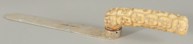A SILVER PAGE TURNER WITH CARVED BONE HANDLE, the handle carved as multiple masks, page turner