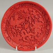 A CHINESE CINNABAR LACQUER DISH, decorated with dragon and phoenix amongst flora, 20cm diameter.