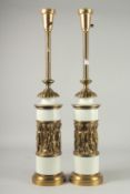 A PAIR OF TALL WHITE PORCELAIN AND BRASS LAMPS with a band of cupids. 27ins high.