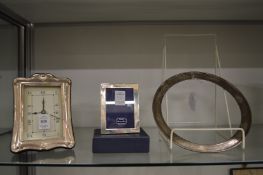 A silver mounted desk clock, small silver photograph frame and a silver circular frame.
