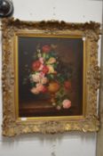 Still life of flowers in a vase on a ledge in a decorative gilt frame.