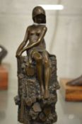 A small bronze of a female semi nude seated on a tree stump.