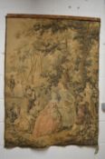 A machine made tapestry wall hanging depicting figures in a garden setting 130cm high x 95cm wide.