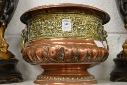 An embossed copper and brass pedestal jardiniere with lion mask handles.