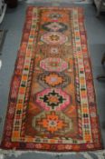 A Persian hall carpet, pink ground with geometric medallions 218cm x 90cm.
