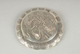 A CHINESE SILVER CIRCULAR COMPACT with a figure on a pathway beside a building. 3.5Iins diameter.