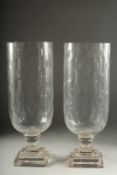 A PAIR OF GLASS STORM LANTERNS on square stepped bases. 15ins high.
