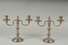A PAIR OF SILVER TWO LIGHT CANDLESTICKS on circular bases. 9ins high.