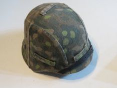 A reproduction WWII German M42 helmet with an SS dot camo helmet cover, with liner and chin strap.
