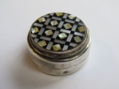 A white metal pill pot set with onyx and mother of pearl having Arabic hallmarks, 3.5cm dia.