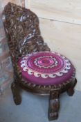 A contemporary carved Indo-Asian style low fireside chair having purple embroidery seat with fire