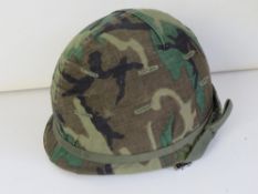 A US M1 Para helmet with a 1969 ERDL cover and a foliage band.
