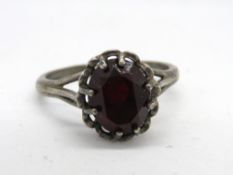 A white metal ring having central red stone, no apparent hallmarks, size O.