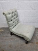 A low fireside chair upholstered in pale green fabric raised over brass and ceramic castors having