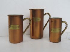 A set of three graduated measuring jugs in brass and copper.