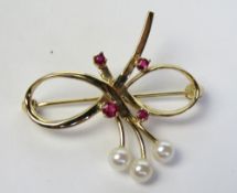A 10ct gold brooch in the form of a bow with pearl 'mistletoe', four round cut rubies over,