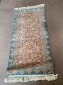 A wool rug in green and sand ground measuring 68 x 134cm.