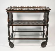 An oak two tiered dinner trolley with a glass top and cane work tier and drop sides together with