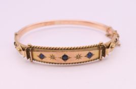 A 9 ct gold, diamond and sapphire bangle form bracelet. 6 cm internal diameter. 9.