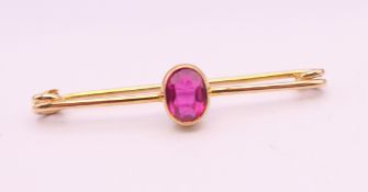 An unmarked gold bar brooch set with a red stone. 4.5 cm long. 2.4 grammes total weight.