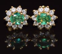 A pair of 18k gold earrings each set with an oval cut emerald of approximately 0.4ct surrounded by