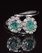 An 18ct white gold ring set with two oval cut emeralds surrounded by diamonds, 3.4g, size L