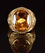 An 18k gold ring set with an oval cut synthetic yellow sapphire within embossed foliate shoulders,