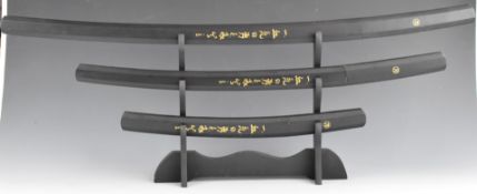 A graduated set of three Japanese Samurai swords with wooden handles and scabbards, largest 97cm