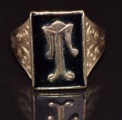 A 9ct gold ring set with onyx and a gold letter T, with scrolling decoration to the shoulders, 5.6g,
