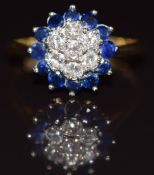 An 18ct gold ring set with seven diamonds surrounded by sapphires in a cluster, 4.4g, size P
