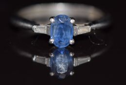 A platinum ring set with an oval cut sapphire and a baguette cut diamond to each shoulder, 3.7g,