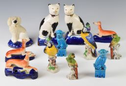 A collection of Staffordshire ware including greyhounds and cats, two pairs of porcelain parrots and