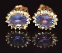 A pair of 18k gold earrings each set with an oval cut tanzanite of approximately 0.65ct surrounded