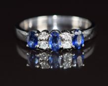 An 18ct white gold ring set with three oval cut sapphires, each approximately 0.2ct and four round