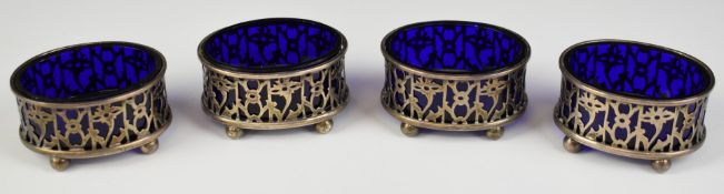 Set of four George V hallmarked silver open salts with blue glass liners and raised on four ball