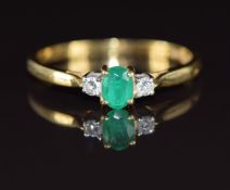 An 18ct gold ring set with an oval cut emerald of approximately 0.3ct and two diamonds, 2.1g, size