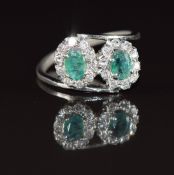 An 18k white gold ring set with two oval cut emeralds each approximately 0.3ct, surrounded by