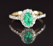 A 14ct gold ring set with an oval cut emerald of approximately 0.78ct surrounded by diamonds