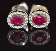 A pair of 18k white gold earrings each set with an oval cut ruby of approximately 0.3ct surrounded